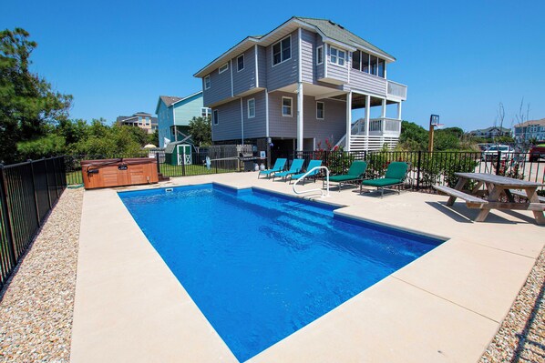 A rectangular swimming pool with a wooden hot tub, surrounded by a black fence and a patio area with green lounge chairs and a picnic table. - Oceanside, Private Pool, Hot Tub, Close to Beach, WW874, Whalecome Aboard (Corolla)