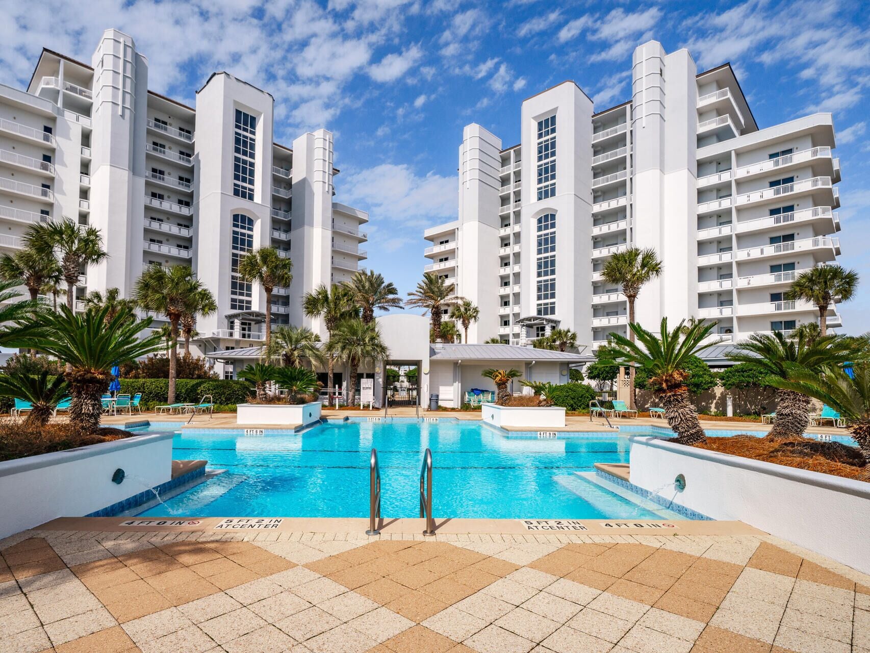 A modern hotel with a central pool surrounded by palm trees and lounge chairs.