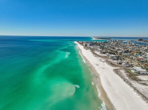 Vista aérea de un pueblo costero con una extensa playa de arena y aguas turquesas cristalinas.