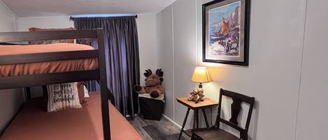 Una habitación con literas, una silla, una lámpara, un cuadro enmarcado y una luz en el techo.