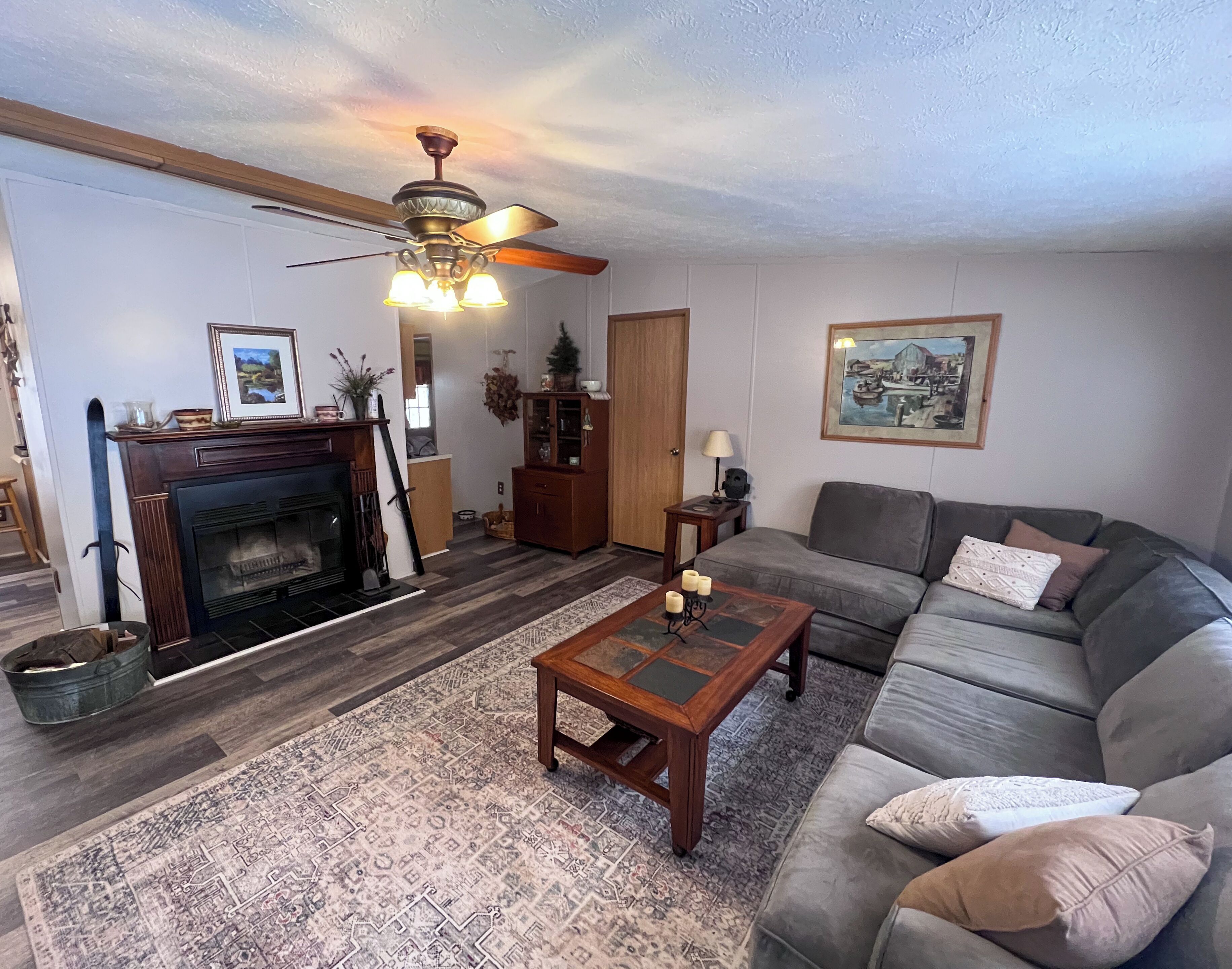 A living room with a fireplace, a sofa, a coffee table, a ceiling fan, and a painting on the wall.