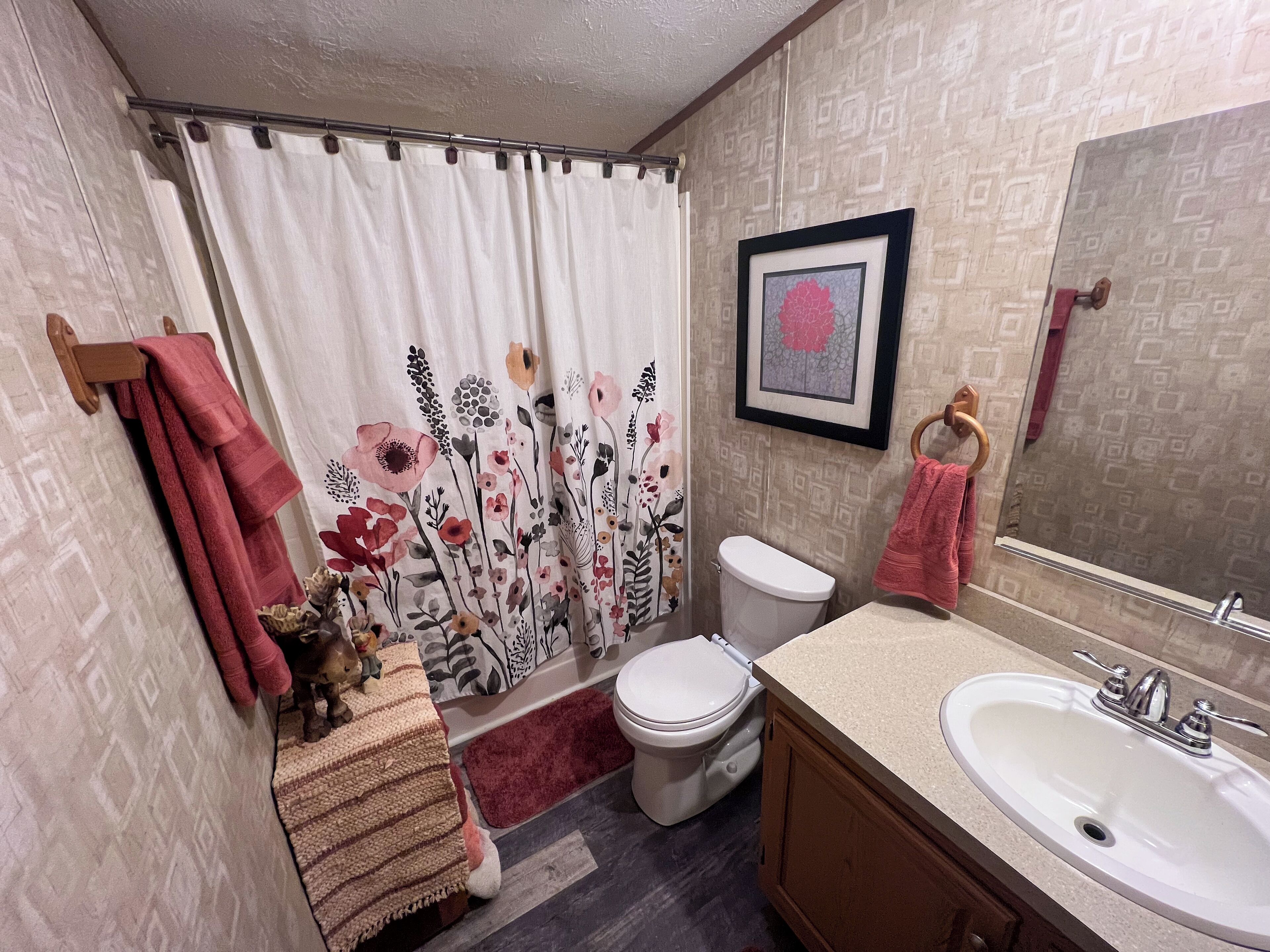 Une salle de bain équipée de toilettes, d’un lavabo et d’un rideau de douche orné de motifs floraux.
