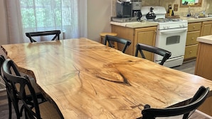 Een eetruimte met een grote houten tafel, zwarte stoelen, een keuken met houten kasten, een magnetron en een fornuis.