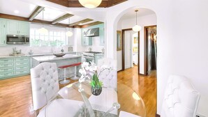 A modern kitchen with wooden beams, a dining area with white chairs, and a view to the living room. - 5-Min Walk To Rose Bowl - Luxe Estate! (Pasadena)