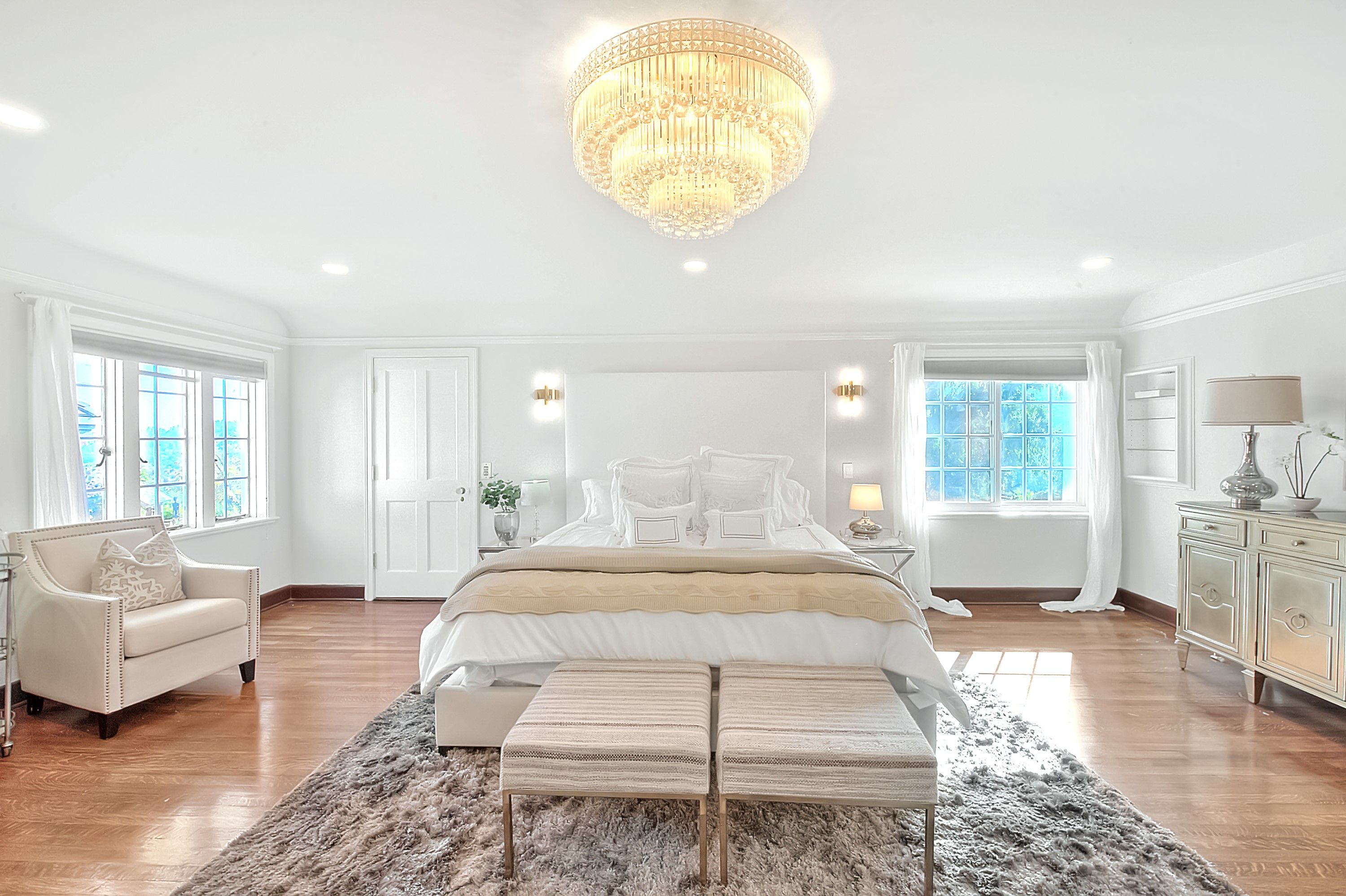A spacious bedroom with a large bed, a chandelier, and a view of the outdoors through the windows.