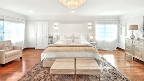 A spacious bedroom with a large bed, a chandelier, and a view of the outdoors. - 5-Min Walk To Rose Bowl - Luxe Estate! (Pasadena)