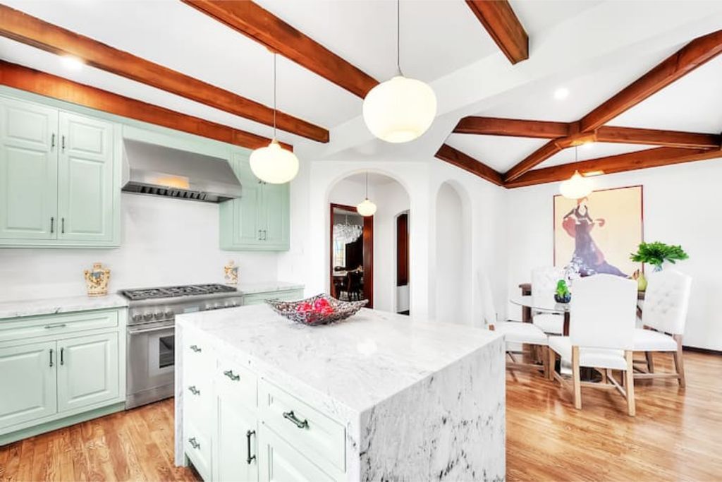 A kitchen with wooden beams, a marble island, and pendant lighting.
