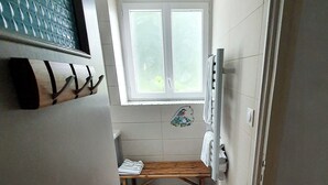 Ein schmaler Gang mit einer hölzernen Bank, einem Fenster mit Milchglas und einem Handtuchhalter.