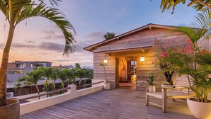 Une terrasse en bois agrémentée de plantes en pot et un petit bâtiment doté d’une porte et de fenêtres.