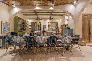 A dining area with a large round table, blue and white checkered chairs, and a rustic ceiling with exposed beams.