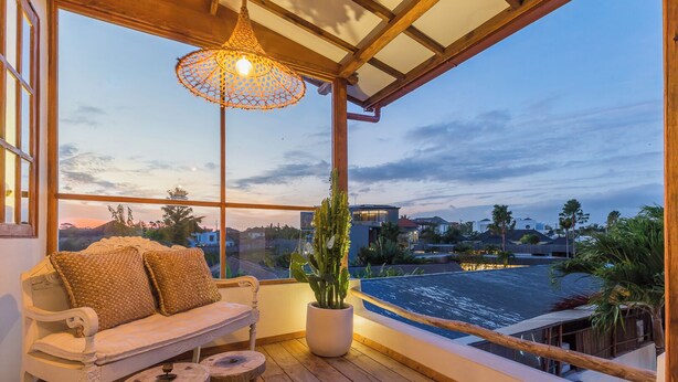 Un balcon avec un plancher en bois, un canapé blanc avec des coussins, un luminaire suspendu et une plante en pot.