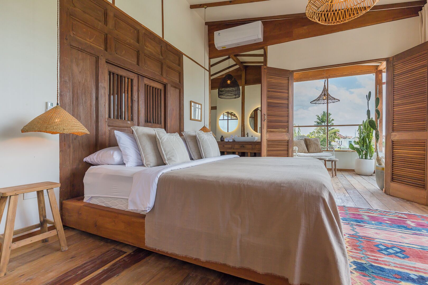Un dormitorio amplio con una cama grande, cabecera de madera y un balcón con plantas en macetas.