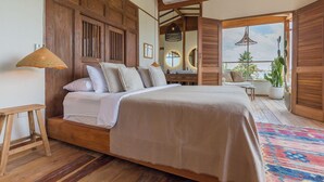 Une chambre spacieuse avec un grand lit, une tête de lit en bois et un balcon agrémenté de plantes en pot.