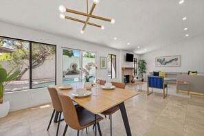 Un comedor moderno con una mesa y sillas de madera, una araña y vistas a una piscina exterior.