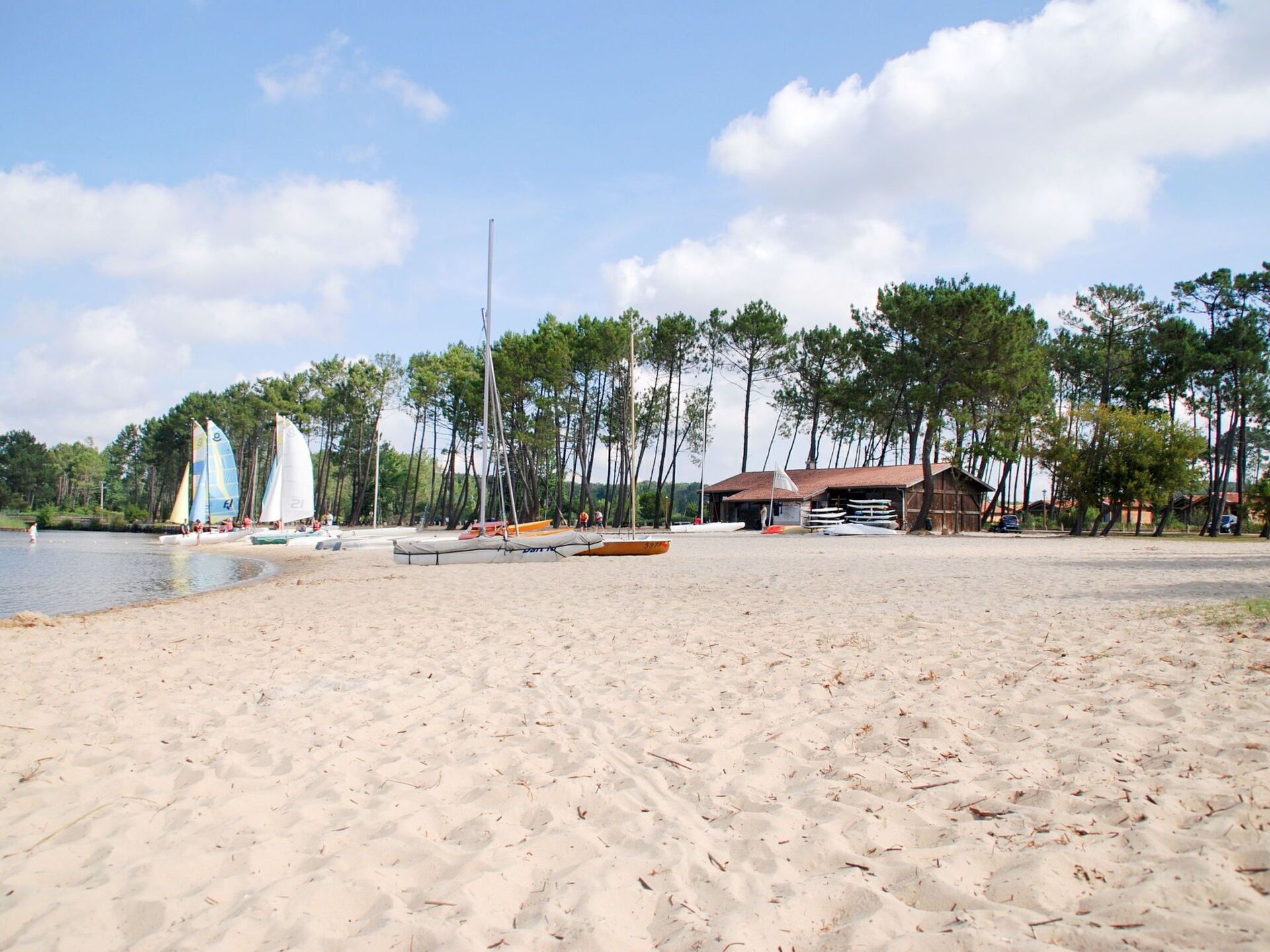 A sandy beach with sailboats and a wooden building in the background.