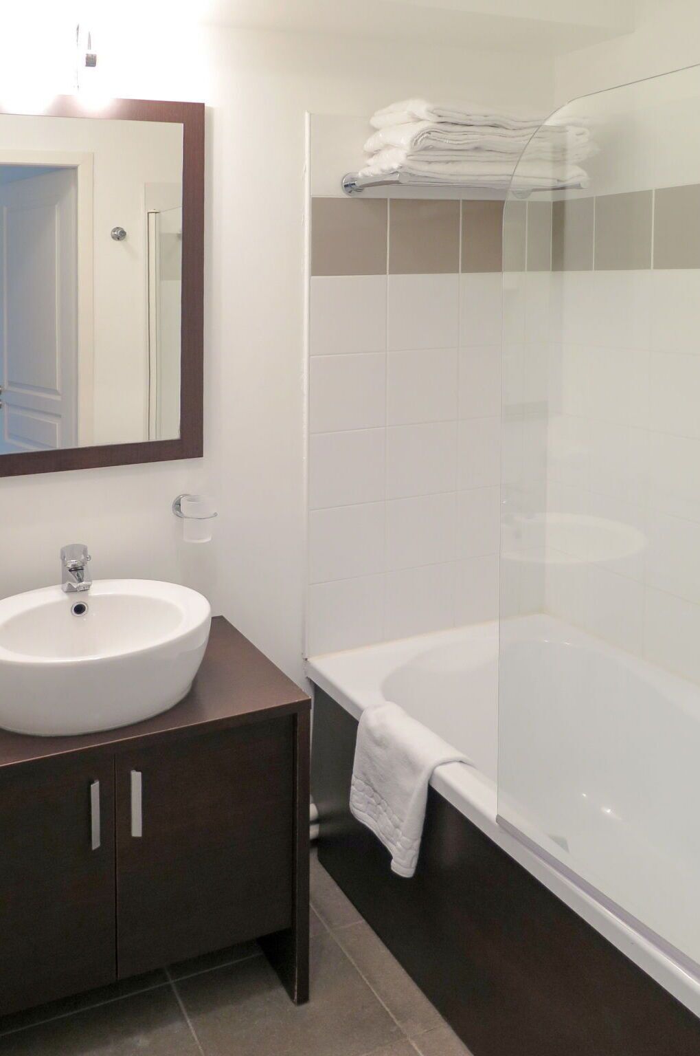 A modern bathroom with a white sink, dark wooden vanity, a glass shower enclosure, and a white bathtub.