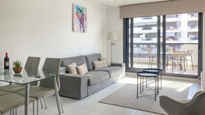 Ett modernt vardagsrum med en grå soffa, ett soffbord i glas och en matplats med stolar.