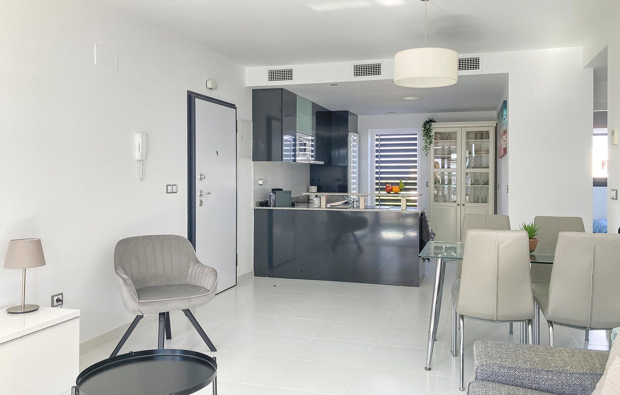 A modern living room with a dining area, a kitchen with a central island, and a door leading to another room.