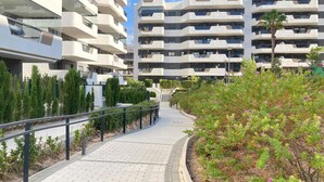 En modern lägenhetsbyggnad med en central gångväg, omgiven av grönska och palmer.