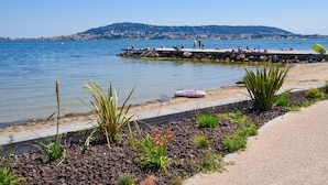 Une promenade en bord de mer, avec une côte rocheuse, une jetée animée et une vue lointaine sur la ville.