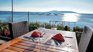 Une table dressée pour deux personnes, avec des verres à vin et des couverts, donnant sur une étendue d’eau et sur une montagne lointaine.