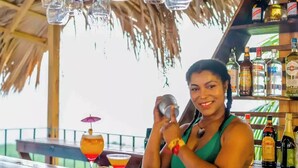 A bartender preparing drinks at a bar with a thatched roof and wooden shelves stocked with bottles. - High Life Resort & Spa (Negril)