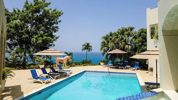 A pool area with lounge chairs and umbrellas, overlooking a beach and ocean. - High Life Resort & Spa (Negril)