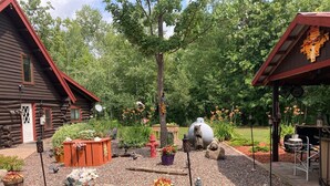 A rustic log cabin with a garden featuring a fire hydrant, bear statues, and various plants. - Custom built log home on 40 acres & in the woods!
Snowmobile right from home! (Barnum)