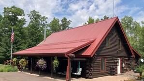 A rustic log cabin with a red roof, a covered porch, and a flagpole. - Custom built log home on 40 acres & in the woods!
Snowmobile right from home! (Barnum)