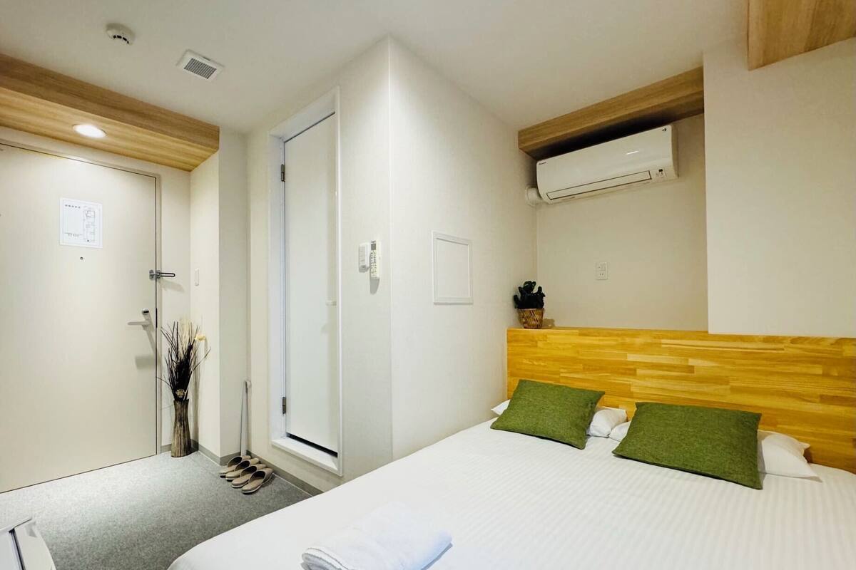 A hotel room with a bed, a wooden headboard, an air conditioning unit, a door, and a small window.