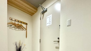 A hallway with a wooden coat rack, a door with a sign, a vase with dried plants, and a pair of slippers on the floor. - Y&Y NAMBA HOTEL Osaka (Osaka)