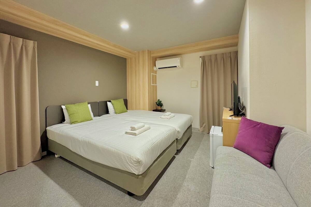 A hotel room with two beds, a desk, a chair, and an air conditioning unit.