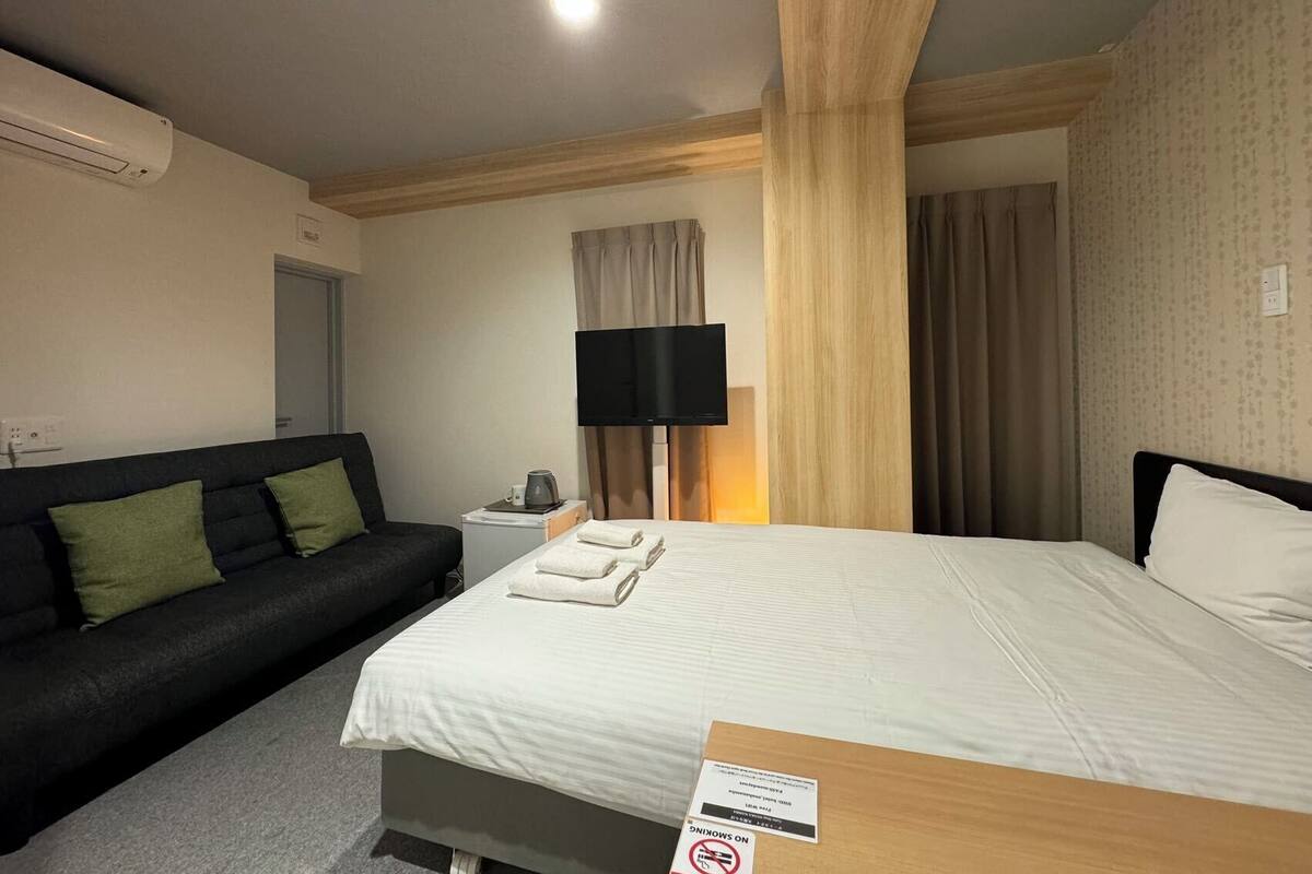 A hotel room with a bed, a sofa, a flat-screen TV, a coffee maker, and a sign indicating no smoking.