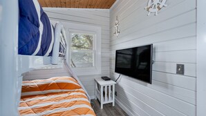 A bedroom with a bunk bed, a television, a small table, and a window with a view of trees.