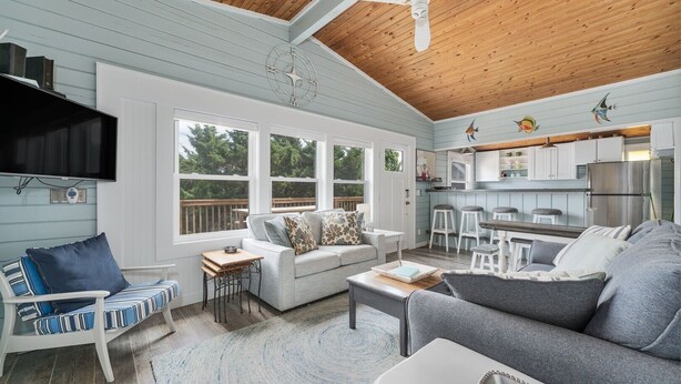 A spacious living room with a large gray sofa, a striped chair, and a wooden ceiling fan.