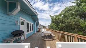 A deck with a wooden table and chairs, a barbecue grill, and a house with teal siding.