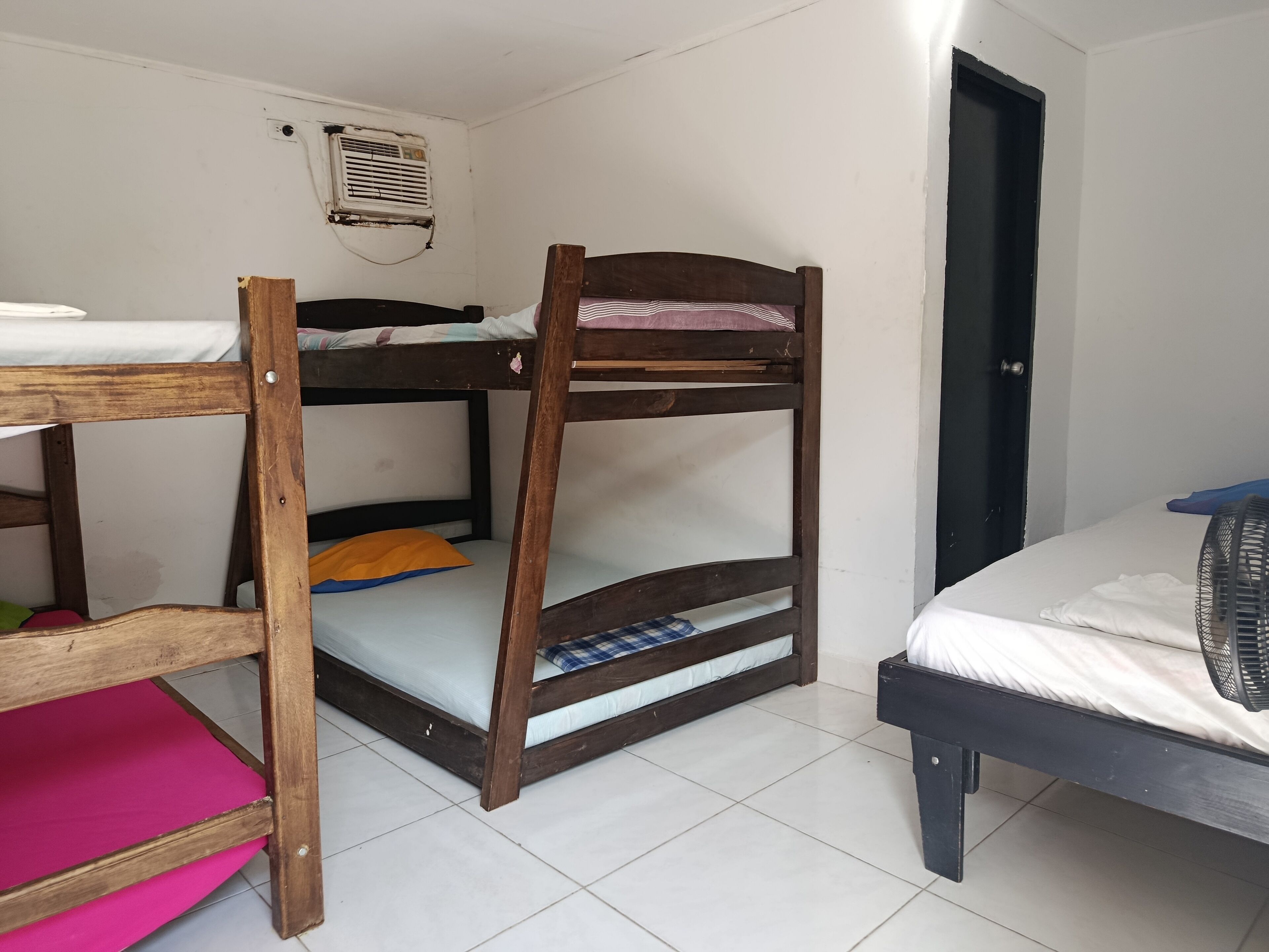 Una cama tipo litera con escritorio y silla, un estante pequeño y un ventilador.