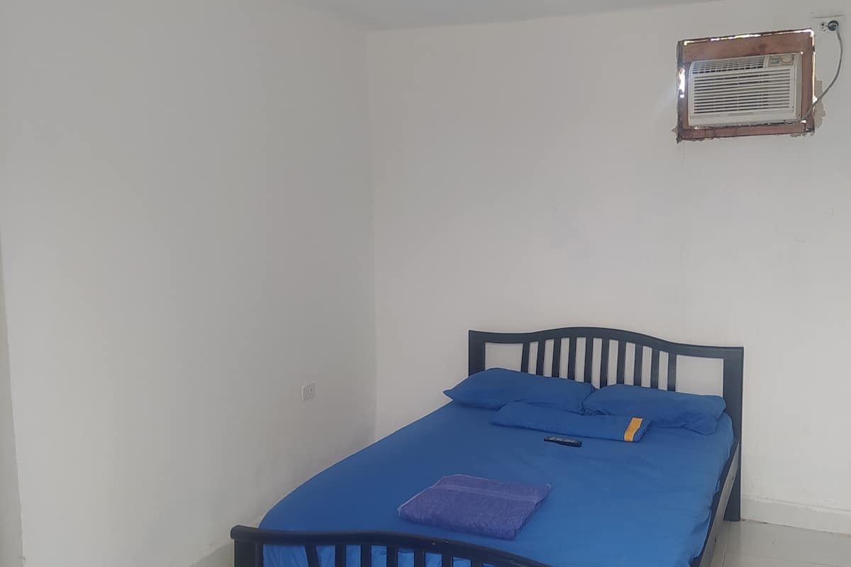 Une petite chambre avec un lit simple, un matelas bleu, une tête de lit en bois et un petit radiateur fixé au mur.
