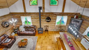 A cozy log cabin interior with a fireplace, leather sofas, and a dining table. - Sugar Grove Log Cabin | HOT TUB + Fire Pit! (Huntingdon)