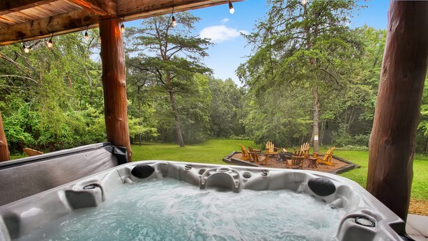 A hot tub with a wooden deck and a view of a grassy area with trees. - Sugar Grove Log Cabin | HOT TUB + Fire Pit! (Huntingdon)