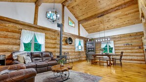 A log cabin interior with a leather sofa, dining table, and chandelier. - Sugar Grove Log Cabin | HOT TUB + Fire Pit! (Huntingdon)