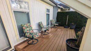 A wooden deck with two chairs and a table, surrounded by a white fence and a green hedge.