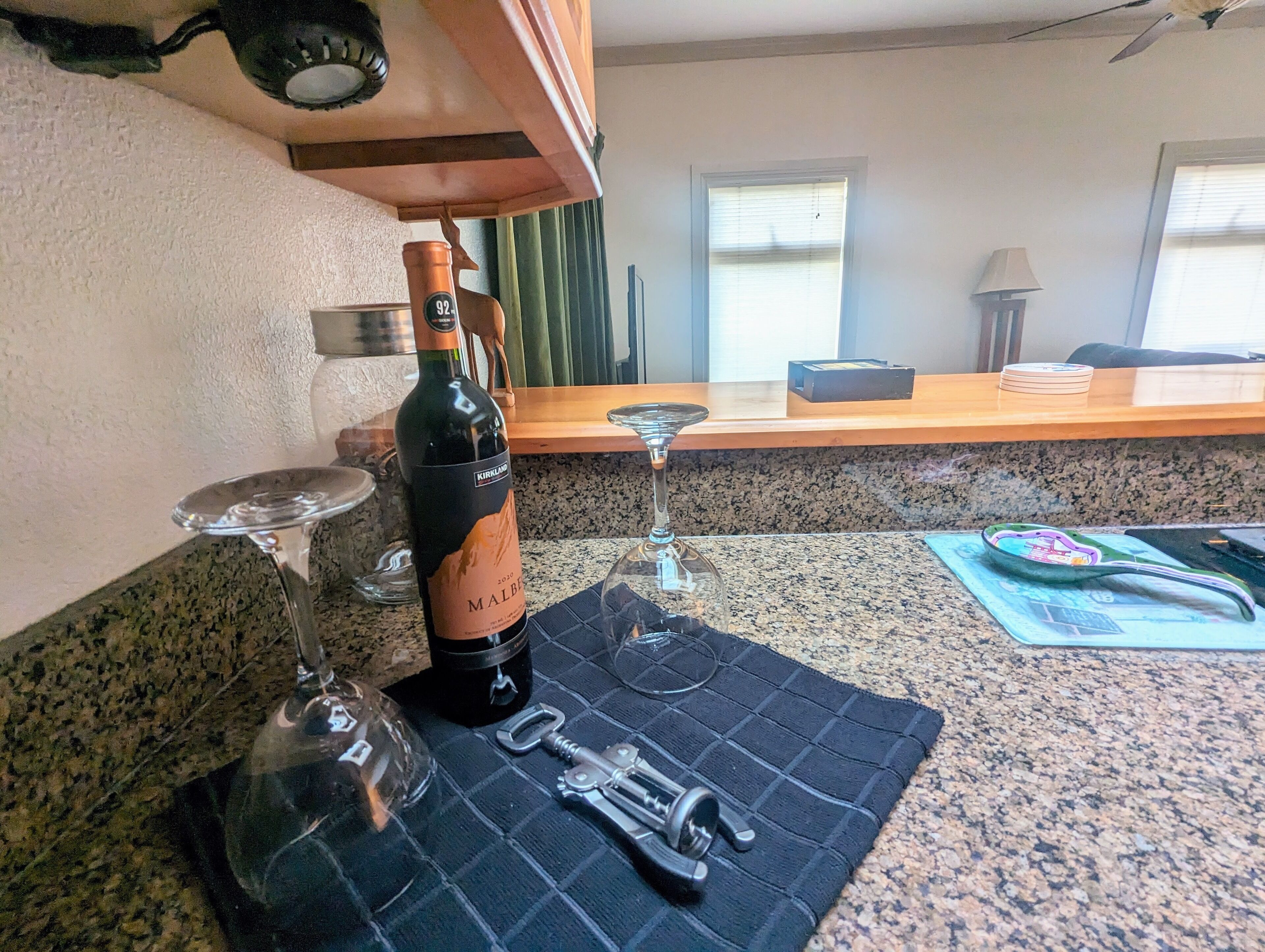 Un comptoir de cuisine avec une bouteille de vin, deux verres à vin et un tire-bouchon, le tout posé sur un set de table.