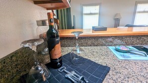 A kitchen counter with a bottle of wine, two wine glasses, and a corkscrew on a placemat.