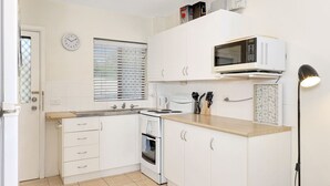 Una cocina compacta con gabinetes blancos, un microondas, una estufa y un lavamanos.
