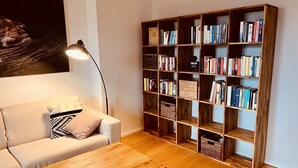 Ein gemütliches Wohnzimmer mit Couchtisch aus Holz, einer beigen Couch, einer Stehlampe und einem großen Bücherregal voller Bücher.