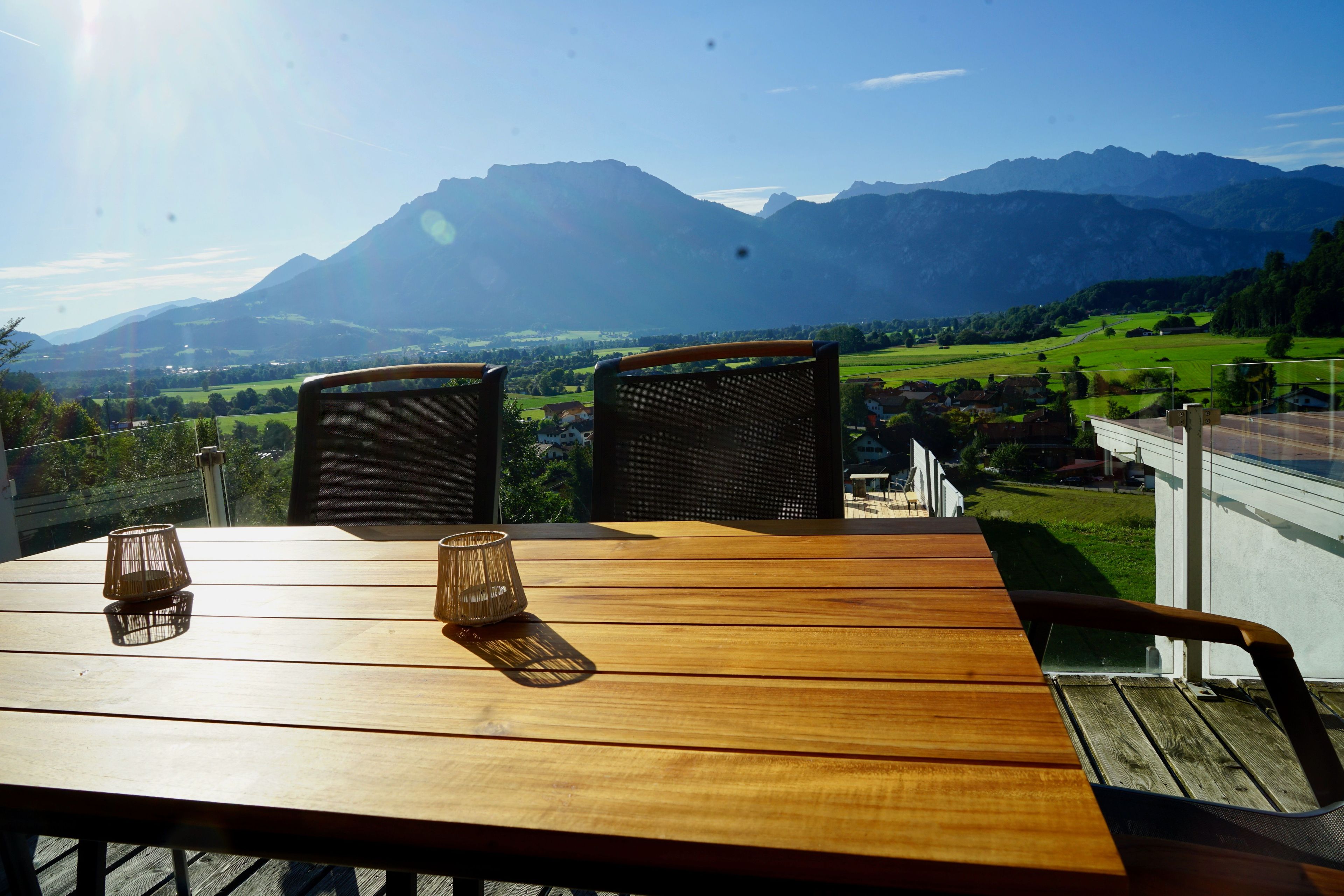Ein Holztisch mit zwei Korbstühlen und zwei Kerzenständern, mit Blick auf eine schöne Berglandschaft und ein grünes Tal.