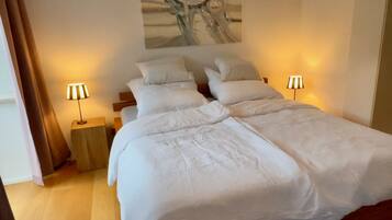 Ein ordentlich bezogenes Bett mit weißen Leinen, zwei Nachttischlampen und einer Traumfänger-Wandkunst.