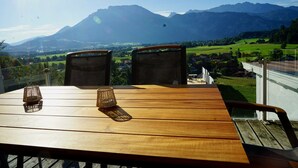 Ein Holztisch mit zwei Stühlen und zwei Kerzenhaltern, mit Blick auf eine Berglandschaft.