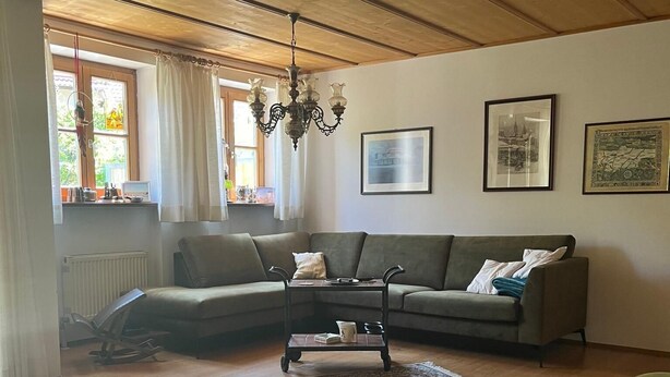 Een woonkamer met een houten plafond, een bank, een bijzettafeltje en een groot vloerkleed.